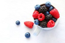 Ripe Blueberries, Raspberries And Blackberries In A White Cup And Next To It.