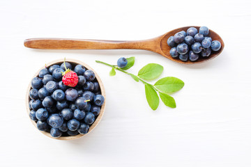 Fresh  blueberries in a wooden cup and a spoon on a white surface of a table. Closeup, top view.