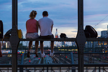 Young couple in love on romantic date sitting on railway bridge with a bottle of wine and watching the sunset over Munich urban city center. Just the two of us.