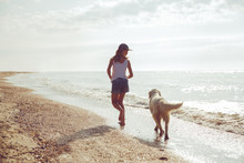 Teenage Girl Running Along A Beach Shore With Her Golden Retriever During The Early Morning.