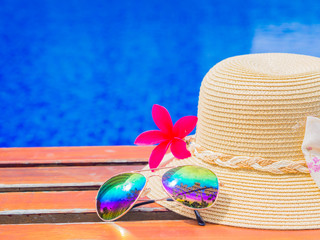 Wall Mural - Sunglasses with summer hat and flowers by the swimming pool. Vacation and relaxation, summer travel concept.