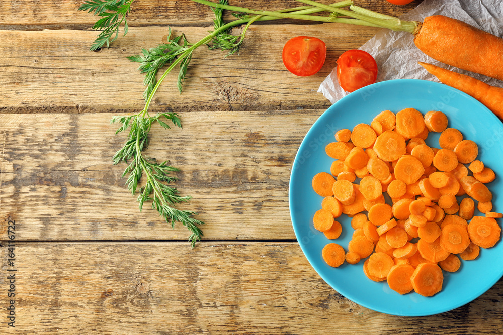 Blue plate with cuts of carrot on wooden background