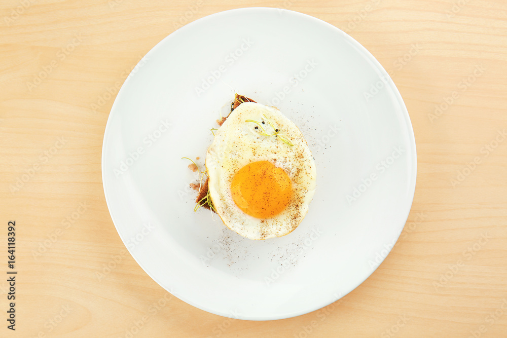 Plate with delicious sunny side up egg and bread slice on wooden background
