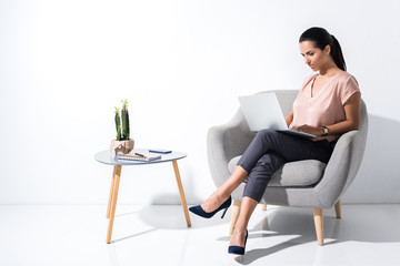 beautiful businesswoman typing on laptop while sitting in chair isolated on white