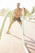 © Addoro - Handsome middle aged man working out on a running track. Healthy adult man doing battle rope exercise. Tanned skin and shirtless middle-aged man.