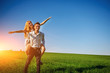 © cezarksv - Smiling Man is holding on his back happy woman, who pulls out her arms and simulates a flight against the background of the blue sky and the green field