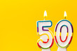 Number 50 birthday celebration candle against a bright yellow background