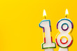Number 18 birthday celebration candle against a bright yellow background