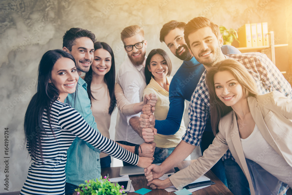 Conception of successful team-building. Close up of businesspeople putting their fists on top of each other on the desktop in nice light workstation, wearing casual clothes - obrazy, fototapety, plakaty 