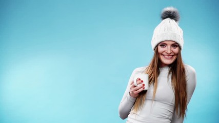 Wall Mural - Woman in winter cap gray sports thermal underwear for skiing training holds mug with tea or coffee warming herself. Winter sport activity. Beautiful long hair sportswoman on blue studio shot, full HD.