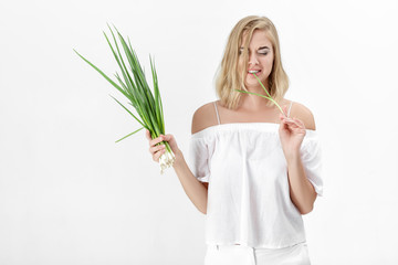 Canvas Print - Beautiful blond woman in a white blouse eating green bitter onion on white background. Health and vitamins