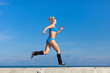 © azazello - Jogging. Young sportswoman in blue sportswear runs along seafront