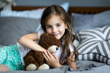 Wall Mural - Cute little girl is playing with a toy bear on the bed