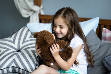 Canvas Print - Cute little girl is playing with a toy bear on the bed