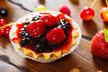 Delicious fruit cake on brown wooden background with strawberries, cherries, currants and raspberries. Beautiful, delightful and healthy desserts