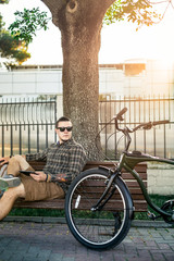 Wall Mural - Young Guy Cyclist Resting On Bench And Using Tablet Communication Connection Digital Devices Technology Concept