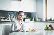 © lenets_tan - Young woman with orange juice and tablet in kitchen.