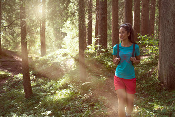 Happy woman with backpack walking on hiking trail path in forest woods during sunny day.Group of friends people summer adventure journey in mountain nature outdoors.Travel exploring Alps,Dolomites