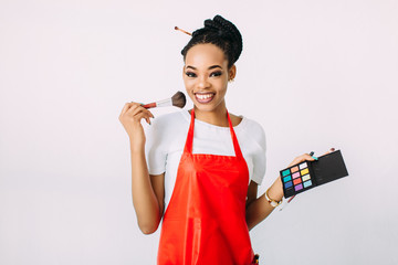 Beautiful young African American beautician woman holding set of make up brushes and eye-shadows