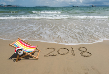 Wall Mural - 2018 written in sand write on tropical beach.Deck chair with Santa Claus sunglasses