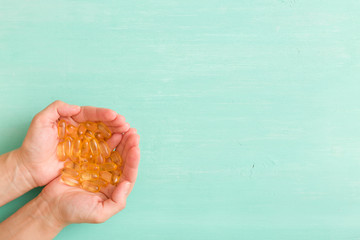 Top view on woman's hands holding pile of capsules Omega 3 on turquoise background.