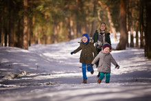 Happy Family Walking In A Winter Forest. Young Woman, Cute Toddler Boy And Kid Boy Smiling And Running On The Snow On A Sunny Day.