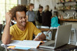 © wayhome.studio  - Joyful African American student sitting at wooden table in cafe surrounded with books, exercise books, laptop holding cell phone in hand looking gladly being happy to recieve congratulations