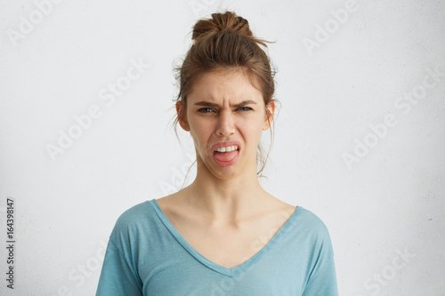 Grumpy femme montrant son dégoût tout en fronçant les sourcils visage de dissatisfaction montrant sa langue Poster Mural XXL