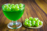 Fototapeta Storczyk - Glass bowl filled with greeen color jelly and gooseberry next to it.