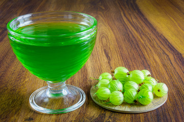 Glass bowl filled with green color jelly and gooseberry next to it.