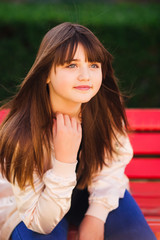 Beautiful girl sitting on red bench on a windy day messing her h