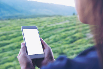 Mockup image of a woman holding and using white smart phone with blank screen at outdoor and green nature background