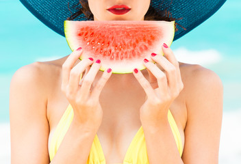 Wall Mural - Summer colors. Girl holding slice of watermelon on the beach with red painted nails. 