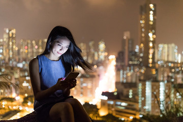 Wall Mural - Woman looking at cellphone with the city background