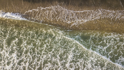 Vista aerea perpendicolare delle onde del mar Tirreno che si infrangono sulla costa. L' impatto con il bagnasciuga crea la schiuma bianca. La spiaggia d'inverno è vuota.