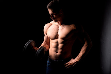 Wall Mural - Strong man with muscular body working out. Weight exercise with dumbbell on black background.