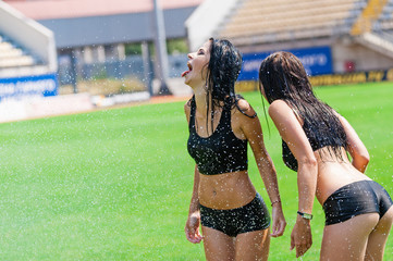 Two charming cheerleaders having fun with irrigation on a football field