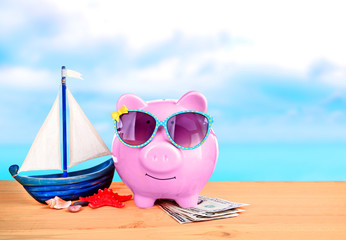 Poster - Pink piggy bank in sunglasses with money, yacht and starfish on wooden table