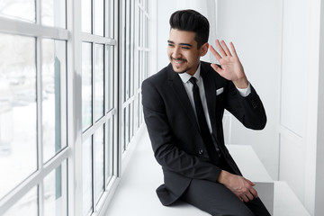 Young smiling businessman sitting on windowsill