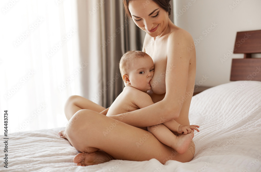 breast-feeding nude Young attractive nude mom breastfeeding hugging her newborn baby smiling  sitting on bed at home. の Stock フォト | Adobe Stock
