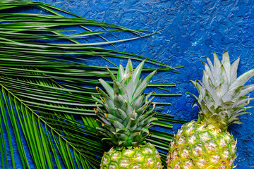  Pineapple and palm branch on blue table background top view