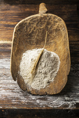 Ancient handmade rustic wooden scoop for flour with wheat ears on a dark natural wooden background. The concept of a home bakery on organic products. Selective focus.