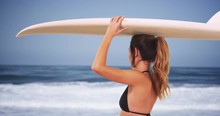Young Caucasian Woman In Black Bikini Holding Surfboard, Looking At Ocean View In Summer. Surfer Girl Posing With Surfboard On Top Of Head, Standing On The Beach By The Waves. 4k 