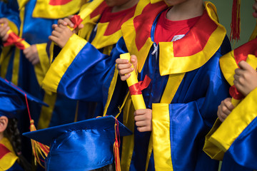 Preschool kid wearing graduation dress and holding diploma closeup