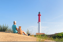 Man And Dog Sitting Near Lighthouse At The Beach