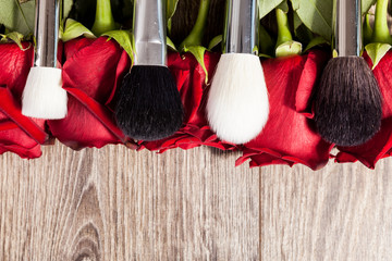 Poster - Conceptual image of make-up brushes next to roses on wooden background