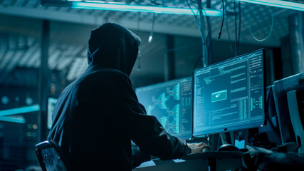 shot from the back to hooded hacker breaking into corporate data servers from his underground hideou