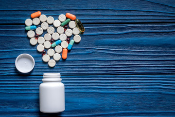 Heart made of pills and pill bottle on blue wooden table background top view copyspace