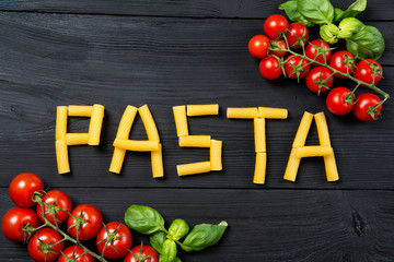 Wall Mural - Word pasta made from tortiglioni pasta macaroni on the black wooden table, ripe cherry tomatoes and basil leaves, top view