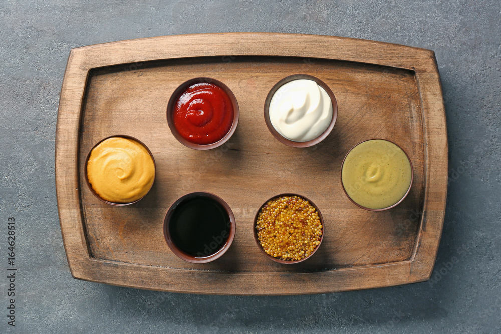 Wooden plate with different sauces on gray background
